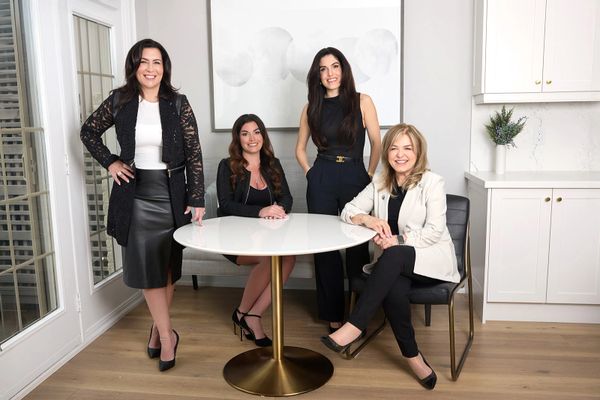 Four professional women posing around a white table in a modern office.