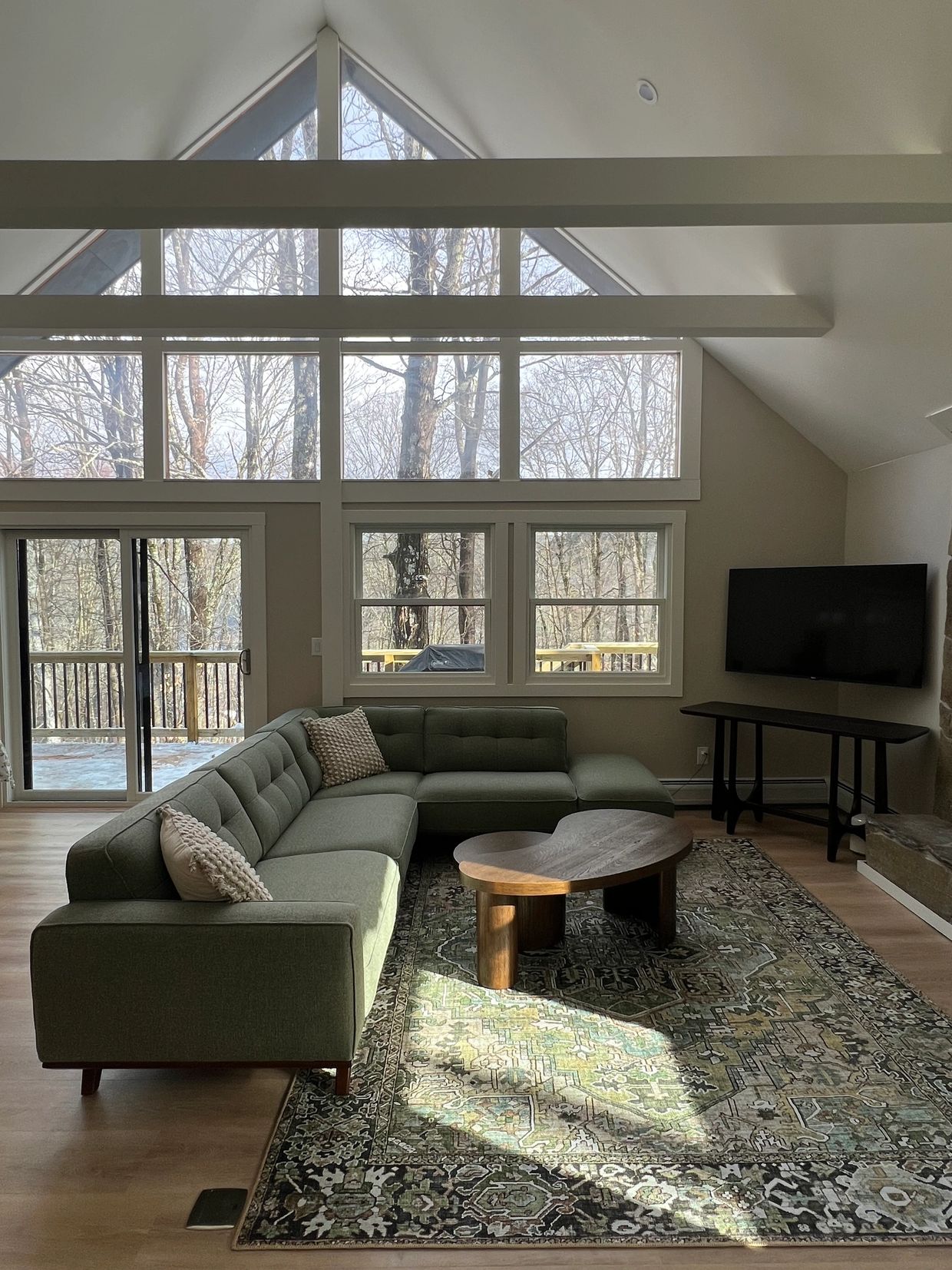 Modern living room with large windows and green sectional sofa.