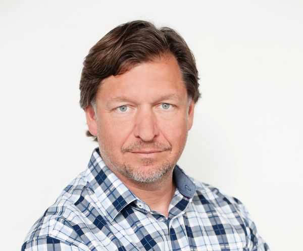 Confident man in a blue plaid shirt posing for a portrait.