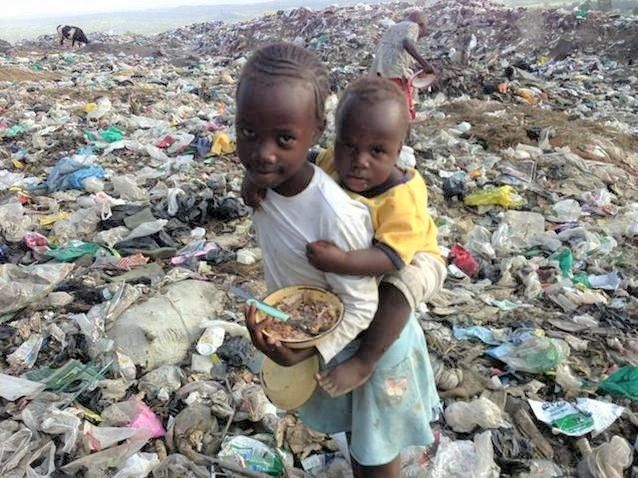Little girl carrying sister with meal in Giotto dump with people  & animals digging in garbage
