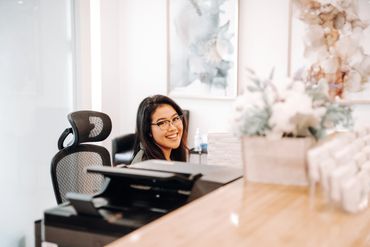 Vancouver bc wellness receptionist with greeting smile sitting at desk.