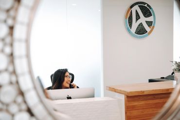Reflection of receptionist talking on phone smiling under company logo.