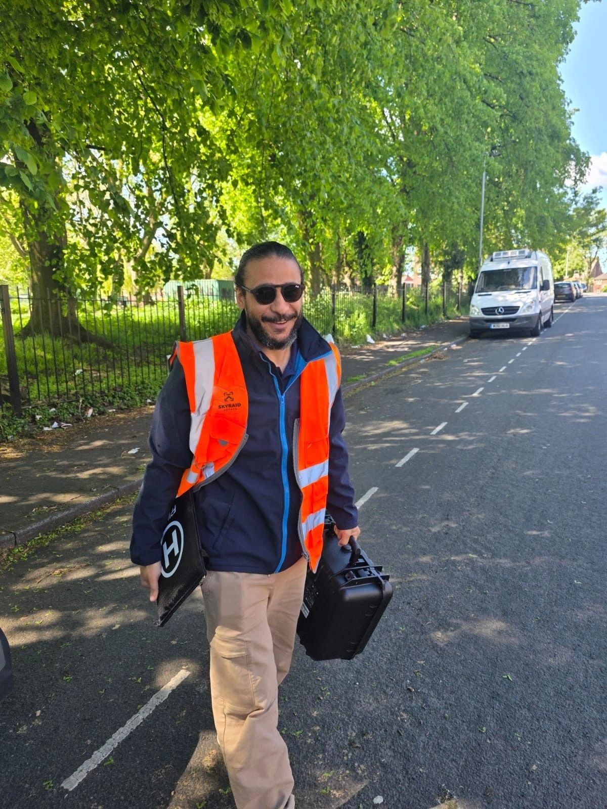 Ahmed Khalifa, founder and pilot of SkyRaid Drones, carrying drone cases along a tree-lined street