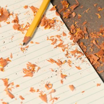 A sharpened yellow pencil on lined paper with shavings scattered around.