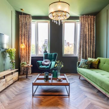 A room with a green couch and chair with hardwood floors