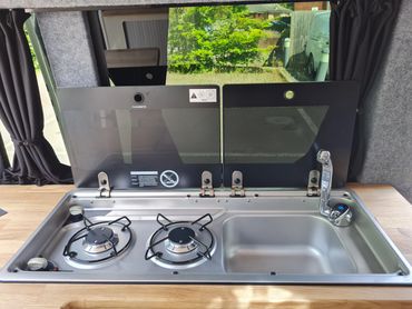 Campervan kitchen with two-burner hob, sink and glass lid, built by Sharkbite Conversions