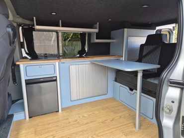 Campervan kitchen with pale blue units and fold-out table
