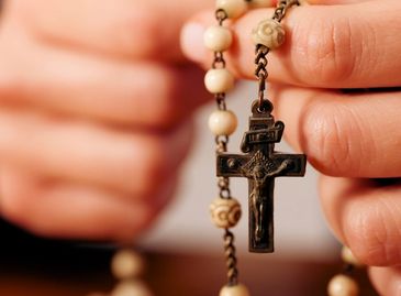 Person holding a rosary with a crucifix in close-up.