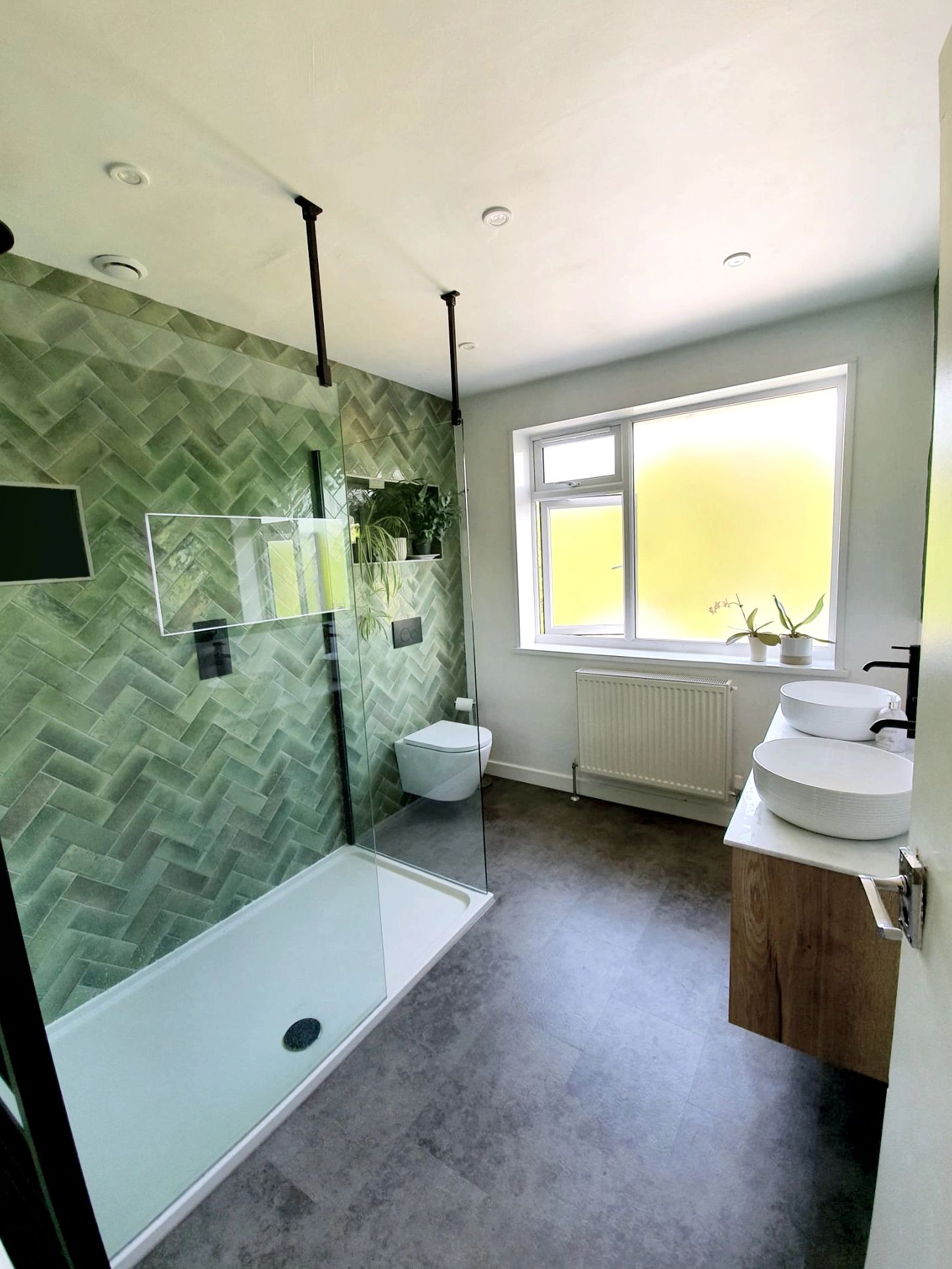 Modern bathroom with green tiled shower and dual sinks under natural light.