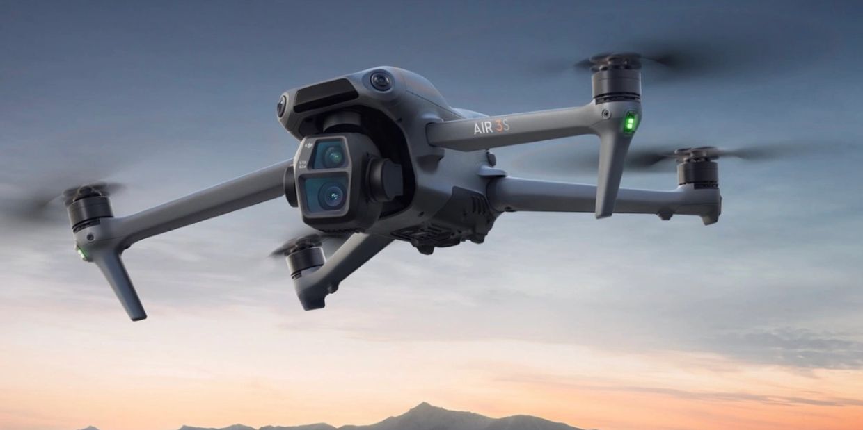 A drone flies over a lake with people and a dog by a white SUV at sunset.