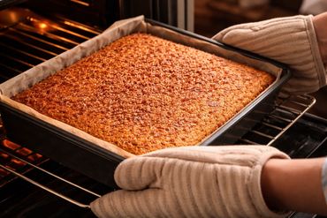 Freshly baked nut-topped cake being taken out of the oven.