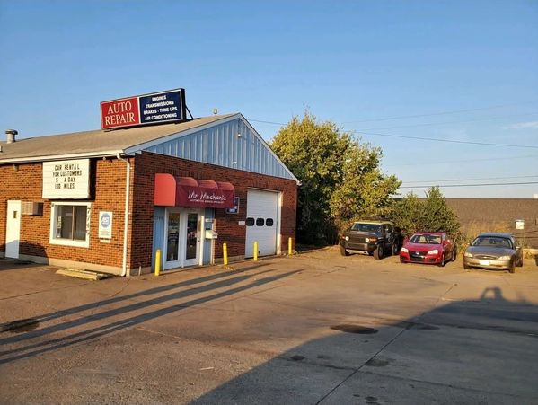 Small auto repair shop with cars parked outside on a sunny day.