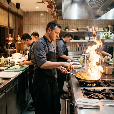 Busy chefs cooking and plating dishes in a professional kitchen with a flaming pan.