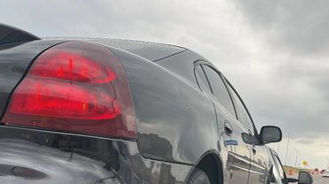 Black car secured on a tow truck on a cloudy day.