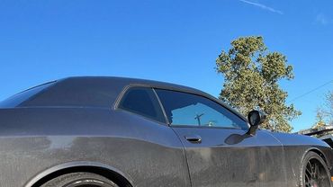 Black muscle car being towed on a flatbed truck under clear blue sky.