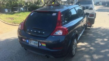 Rear view of a black Volvo C30 with various bumper stickers, parked on a street.
