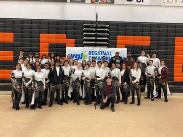 A large group of performers posing in a gym with a championship banner.