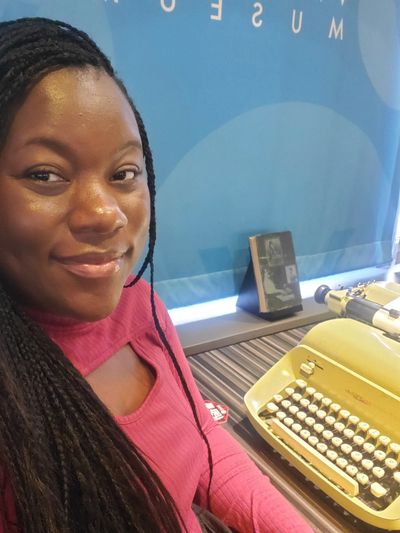 Woman smiling beside a vintage typewriter in a museum.