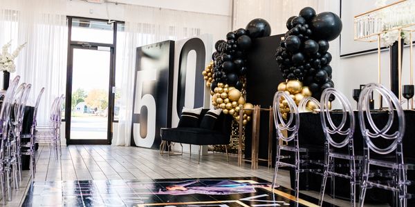 Elegant black and gold 50th birthday party setup with balloons and clear chairs.