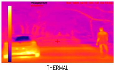 Thermal image showing a person walking near a car on a road at night.