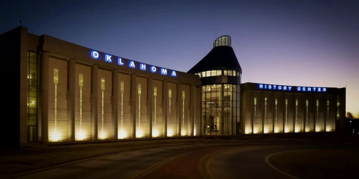 The south side of the Oklahoma History Center at night, illuminated signs and ground lighting.