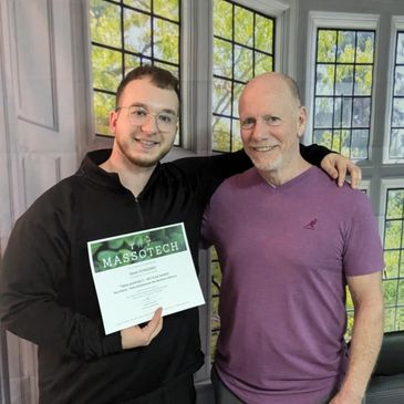 Two men smiling, one holding a Massotech certificate indoors.