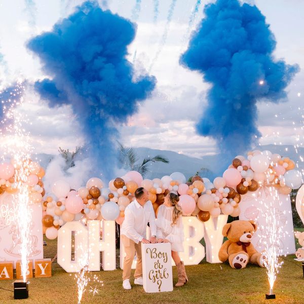 Couple reveals baby's gender with blue smoke and festive decorations outdoors.