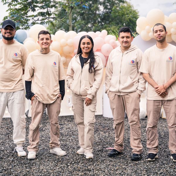 Group of five young adults in matching beige outfits, smiling outdoors.
