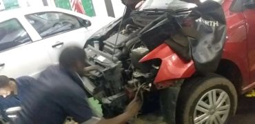 Two mechanics fixing a damaged red car.