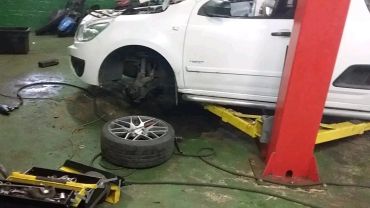 White car on a lift with a removed front wheel in a workshop.