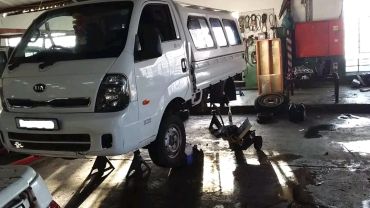 White Kia truck lifted on jacks in a garage.