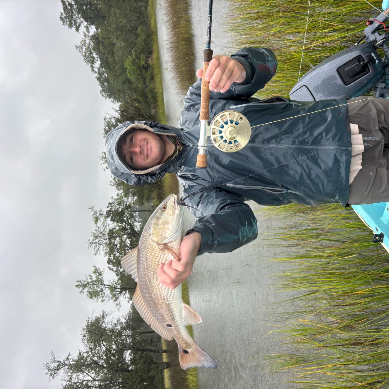 Angler proudly holding a large fish caught in rainy weather.