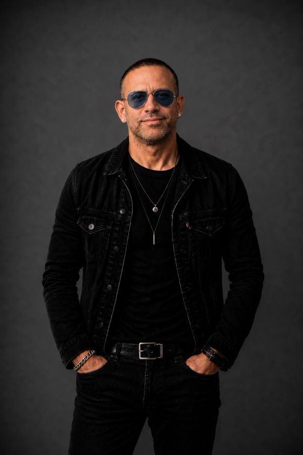 Man in black denim jacket and sunglasses posing confidently.