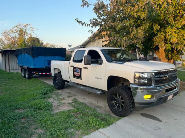 White pickup truck towing a blue trailer parked on a driveway near a house.