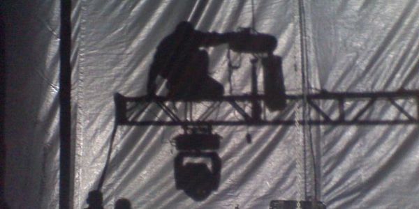 Silhouetted worker adjusting stage lighting from a suspended platform.