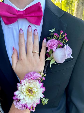 A hand with a ring and floral wrist corsage on a tuxedo with a pink bow tie and boutonniere.