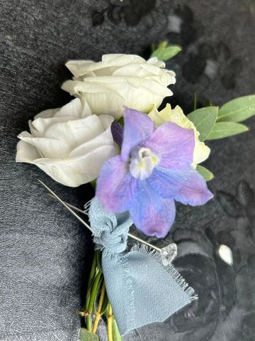 A boutonniere with white roses and a purple flower tied with a blue ribbon.