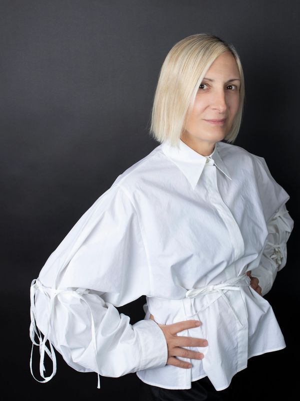 Blonde woman in a stylish oversized white shirt posing confidently.