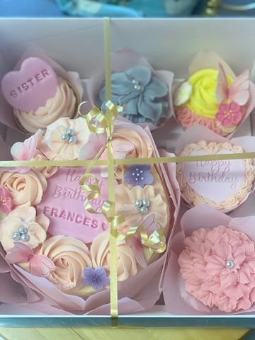 Decorative pastel birthday cupcakes arranged in a gift box with floral designs.