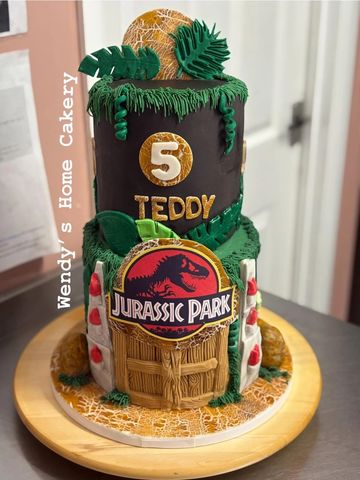 Two-tier Jurassic Park themed birthday cake with dinosaur and jungle decorations.