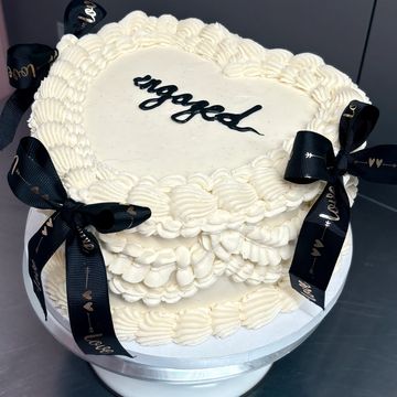 Heart-shaped engagement cake with white frosting and black ribbon bows.