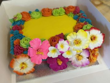Vibrant yellow cake decorated with colorful buttercream flowers and fresh blossoms.