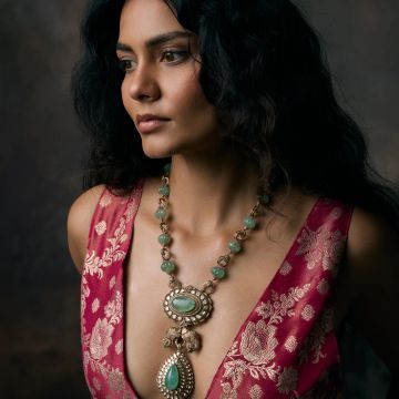 Woman in a red floral dress wearing an intricate green and gold necklace.