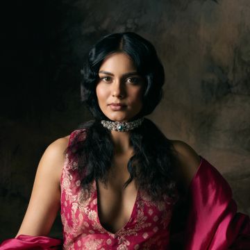 A woman in a deep pink floral dress with a jeweled choker against a dark backdrop.