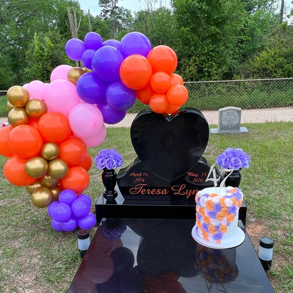Colorful balloon arch and cake at a heart-shaped gravestone memorial.