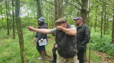 Man using a slingshot in a forest while three others watch.