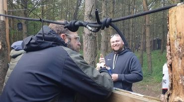Two men chatting outdoors in a forested area.