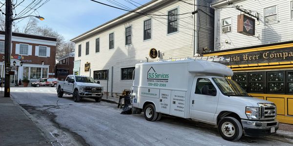 White service van and truck parked on a quiet street with shops.
