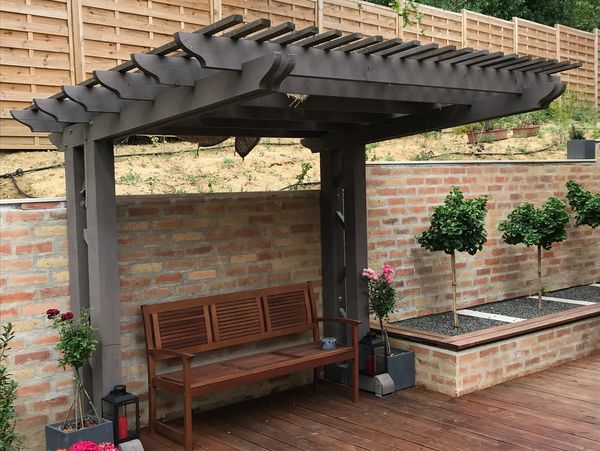 Wooden pergola with bench in a backyard.