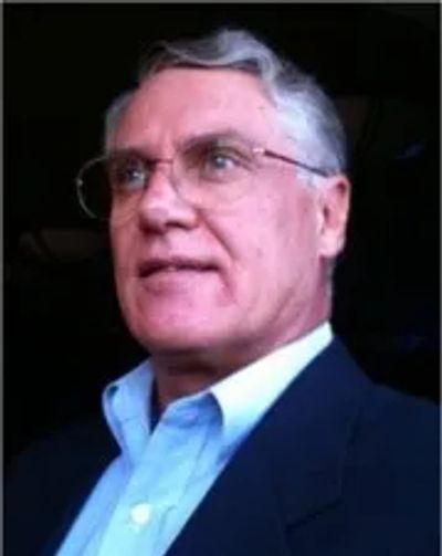 Portrait of an older man in glasses and a suit jacket.